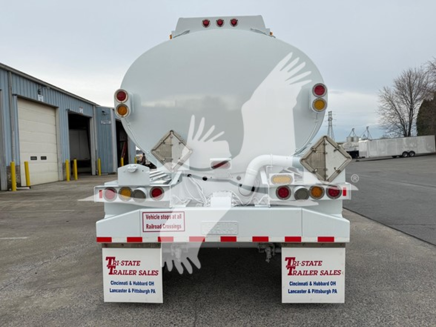 Tank trailer rear showing round tank and rear lights with mud flaps; labels read ‘Tri-State Trailer Sales’ and visible license/stock stickers.