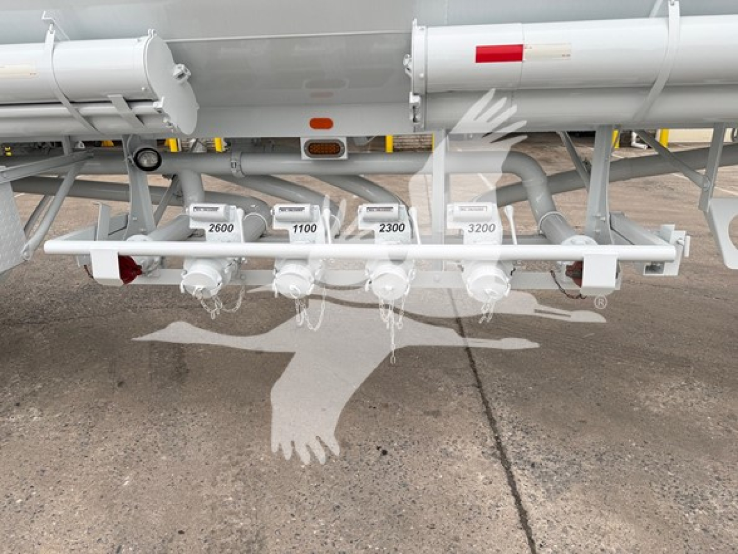 Tank trailer bottom loading manifold with multiple control valves labeled with numbers (2600, 1100, 2300, 3200) and piping underneath and a white painted frame.