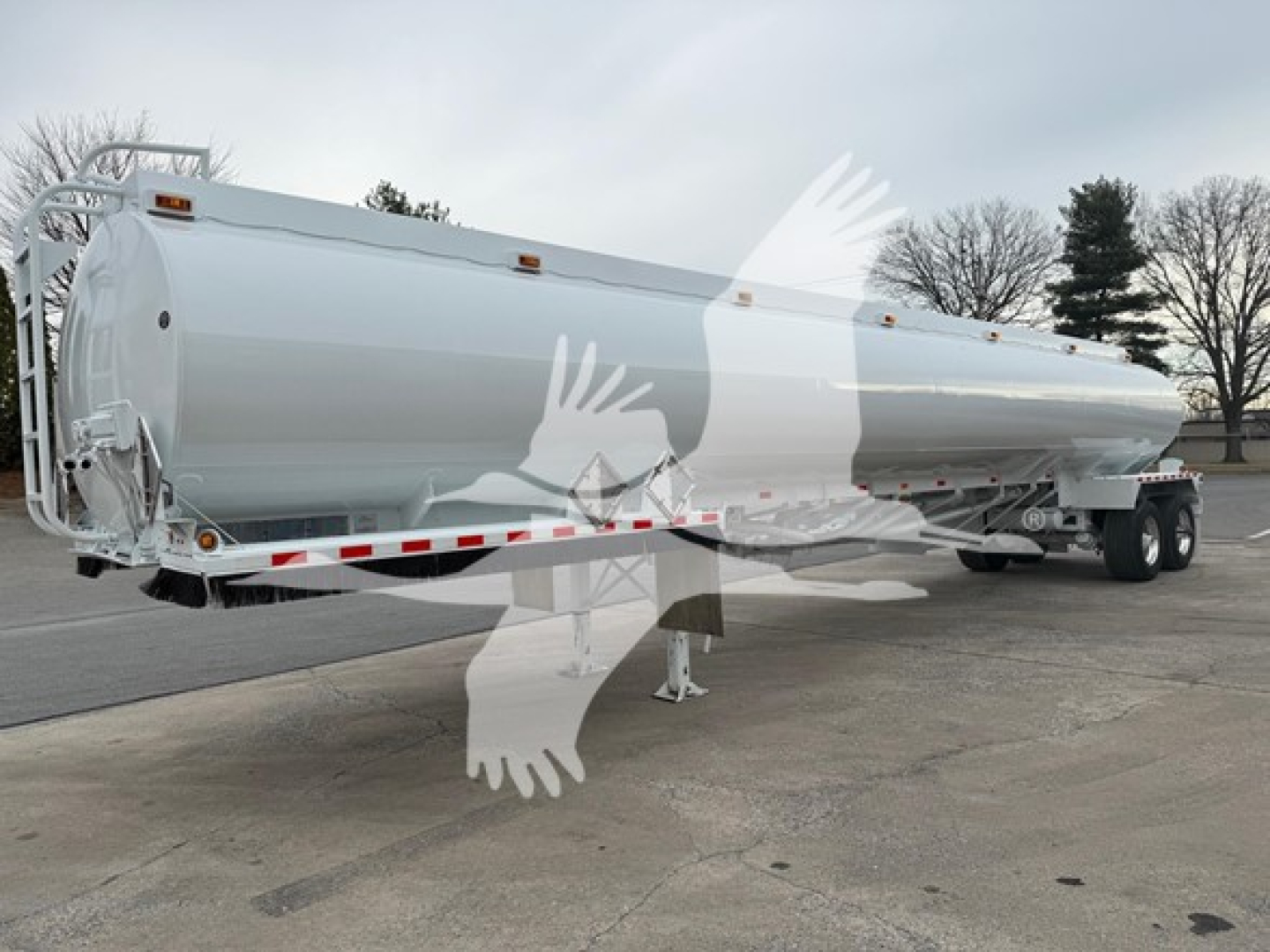 Tank trailer showing a cylindrical Heil trough bottom petro tank mounted on dual-axle trailer with white exterior and safety decals.