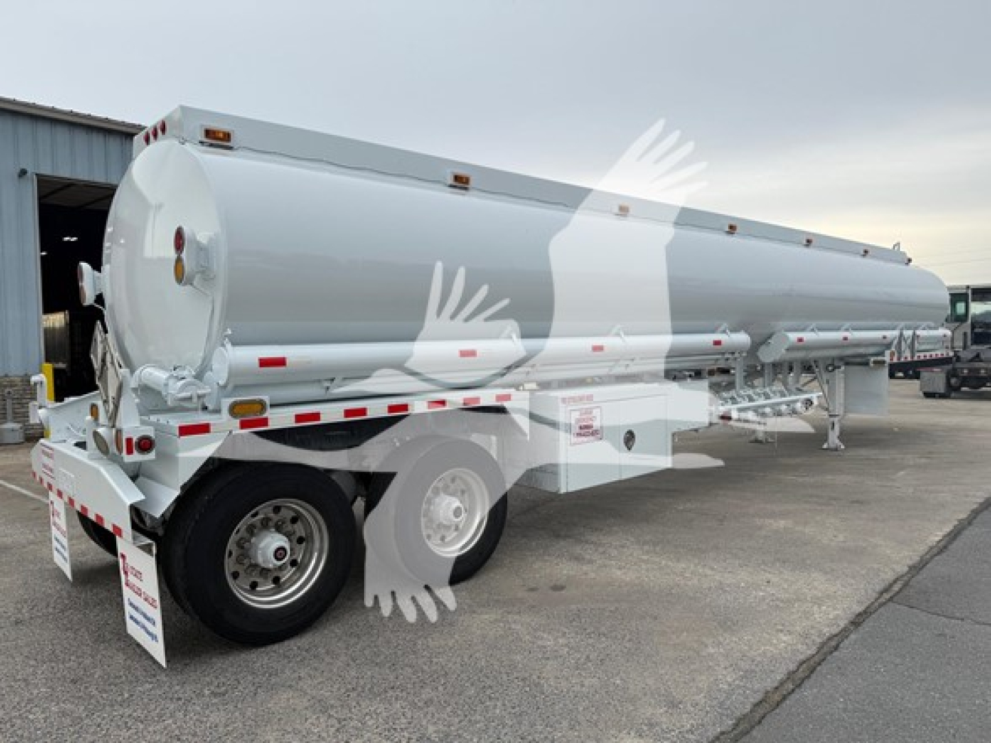 Trough bottom Petro tank trailer in a parking lot showing rear and side with wheels and reflective tape, white cylindrical tank, tail lights.
