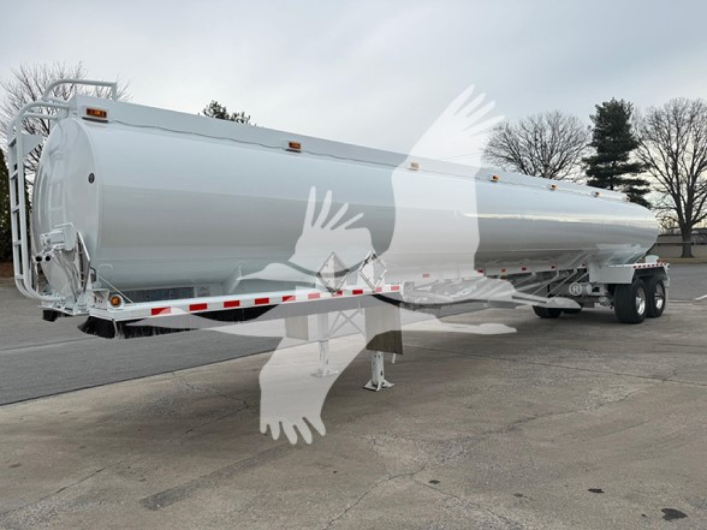 Tank trailer showing a cylindrical Heil trough bottom petro tank mounted on dual-axle trailer with white exterior and safety decals.