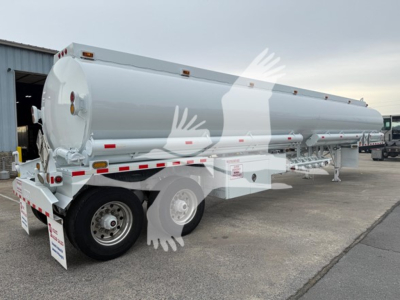 Trough bottom Petro tank trailer in a parking lot showing rear and side with wheels and reflective tape, white cylindrical tank, tail lights.