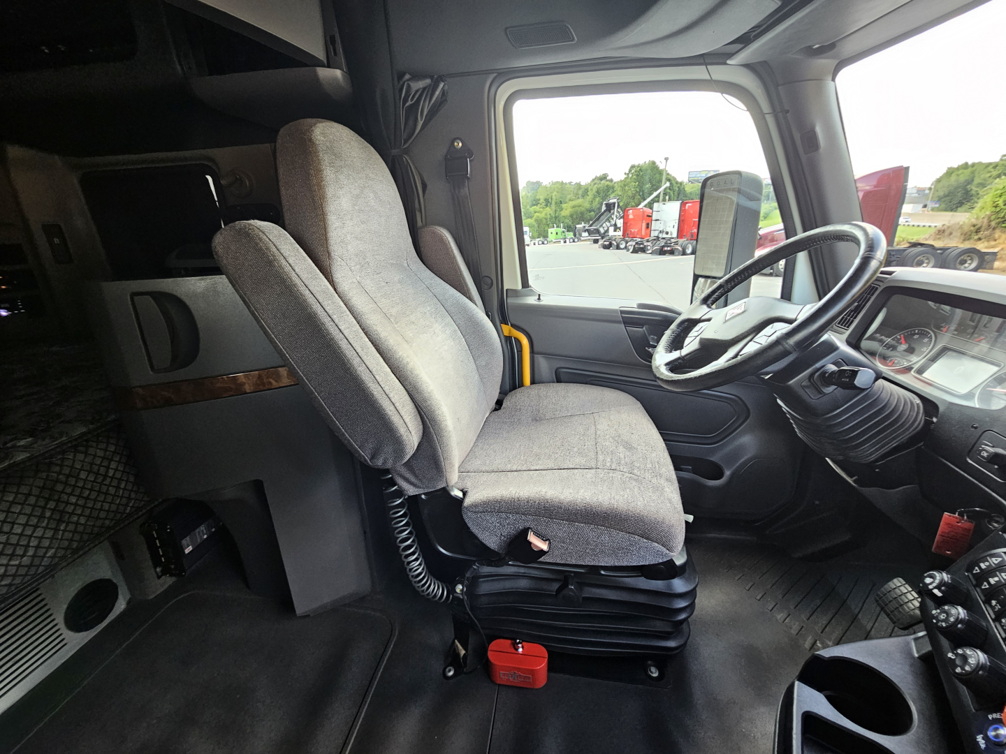 Truck cab interior showing driver seat and passenger seat in front of dashboard; steering wheel, control panels, and side window visible.