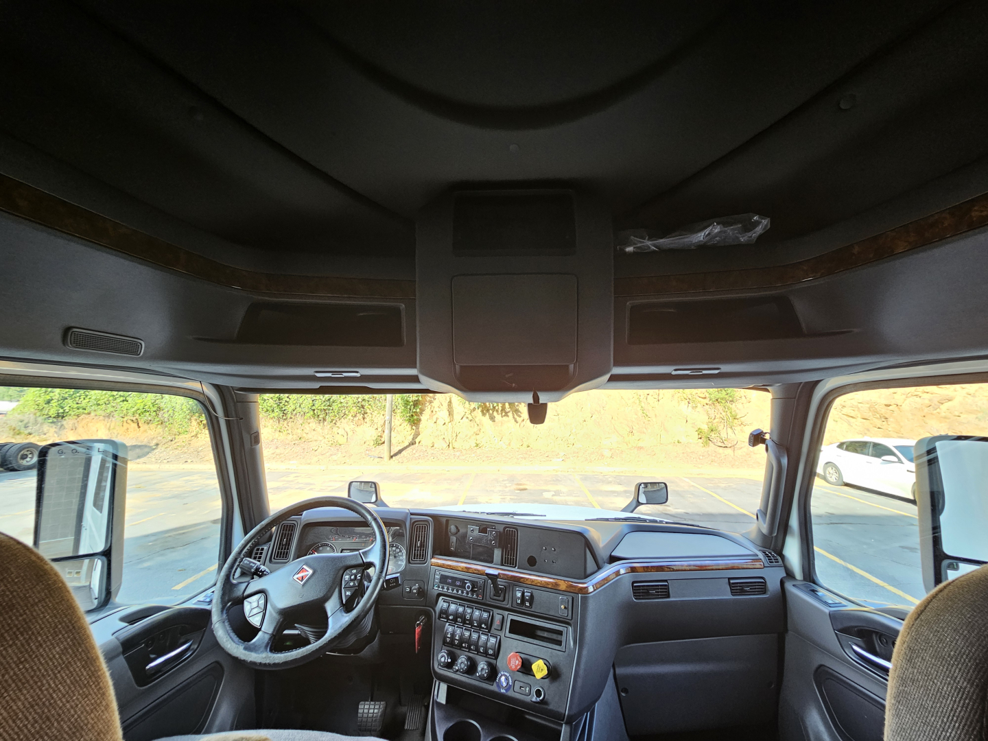Truck cab interior of a 2021 International LT625 sleeper, dashboard with steering wheel on left, center console controls, and large windshield views.