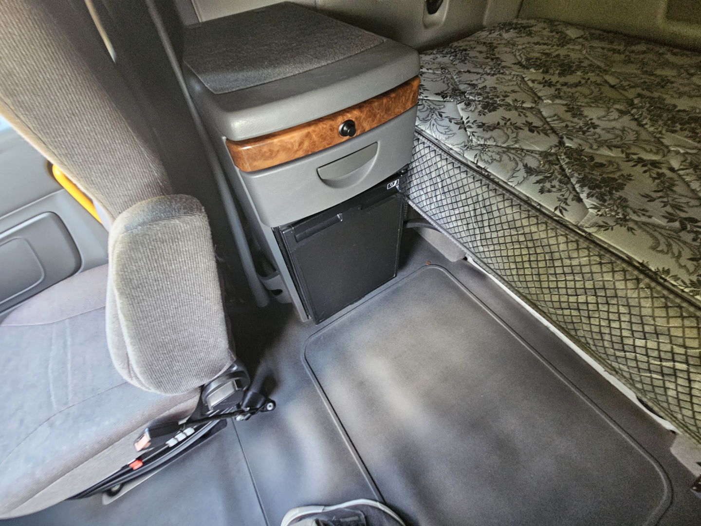 Interior cab view of a 2021 International LT625 truck showing a captain seat, storage drawer, wood trim, and a mattress in sleeper area.
