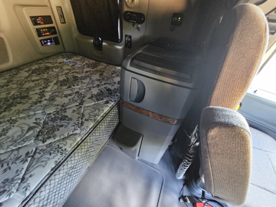 Truck cab interior showing sleeper bed area with floral mattress pattern, center console, and seating in view.