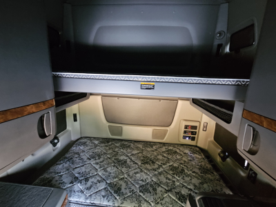Interior sleeper cab bunk area of a 2021 International LT625 with upper bunk and storage shelves. Visible controls on lower right wall, carpeted lower bunk.