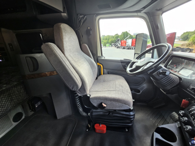 Truck cab interior showing driver seat and passenger seat in front of dashboard; steering wheel, control panels, and side window visible.