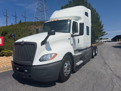 Truck image showing a white 2021 International LT625 conventional sleeper tractor with a high roof, large black grille, side mirrors, and dual rear axles.