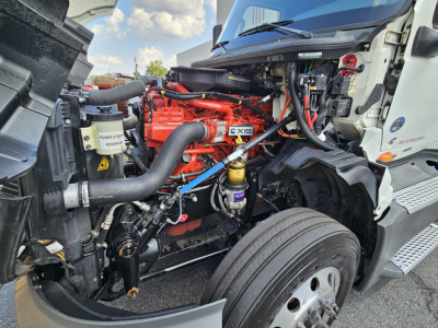 International LT625 engine bay showing orange engine block, hoses, and battery area with coolant reservoir and turbo components.