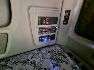 Interior overhead console of a sleeper cab showing switches and a blue digital display panel. Text on panels not fully legible.