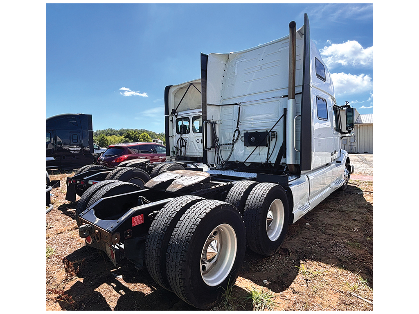 Volvo VNL 860 sleeper tractor rear view showing drivetrain and dual rear axles, trucks in yard.