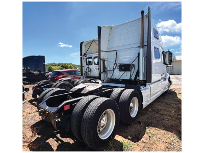 Volvo VNL 860 sleeper tractor rear view showing drivetrain and dual rear axles, trucks in yard.