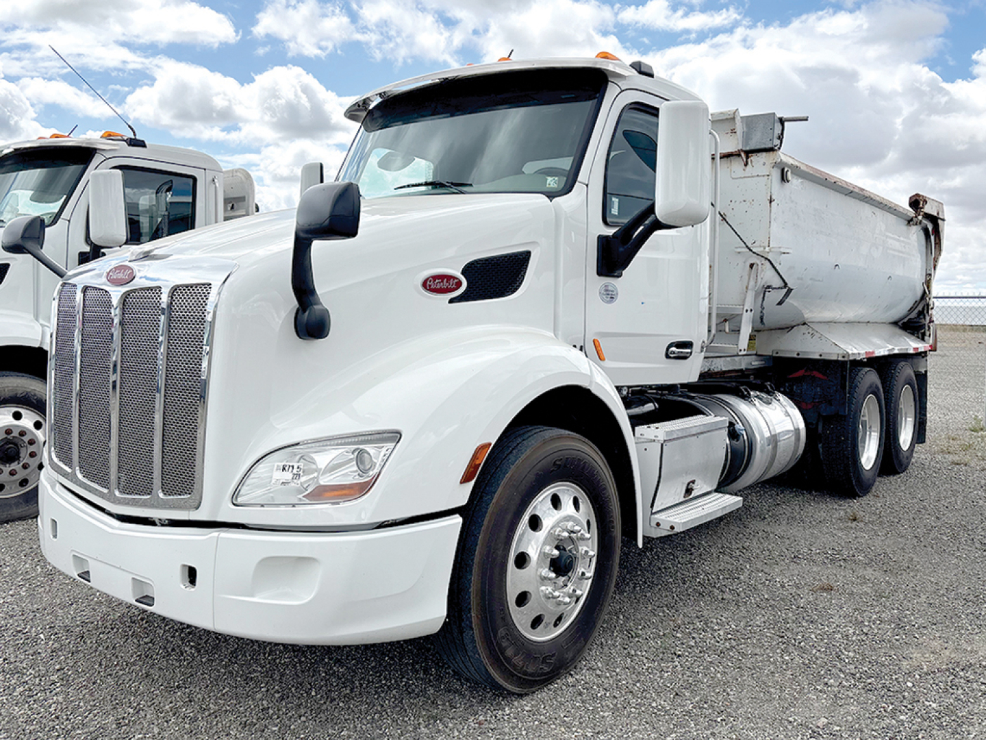Peterbilt 579 dump truck in white with chrome grille and dual rear wheels, side fuel tanks, and dump bed visible.
