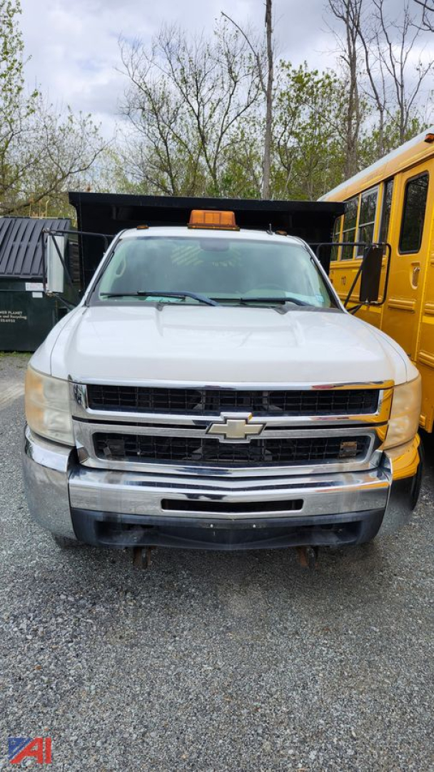 Chevrolet Silverado 3500HD dump truck front view showing grille, bumper, and cab with a roof beacon, adjacent to a yellow school bus.