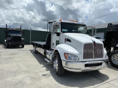 Kenworth T3 series tow truck with white cab and flatbed, front grille, chrome bumper, and orange clearance lights on cab roof.