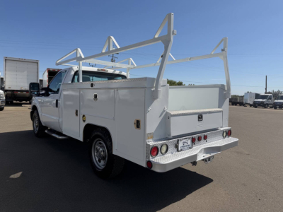 Ford F-250 utility service truck in white with ladder racks and rear cargo box, three-quarter rear view showing service compartments and bumper hitches.