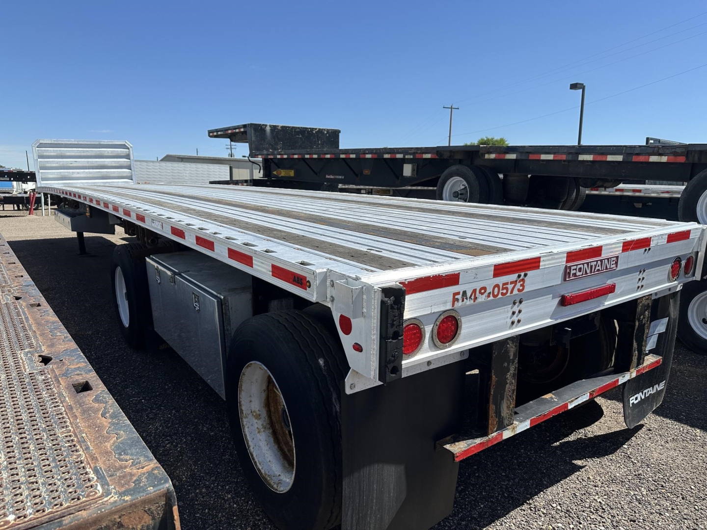 Flatbed trailer showing aluminum deck and dual rear axles with red/white reflective tape and "FRONTRUNNER" branding on fender