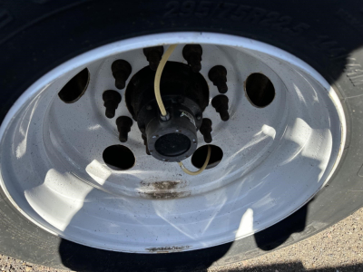 Trailer wheel and tire hub close-up showing steel rim with lug nuts and yellowed air lines against a black tire.