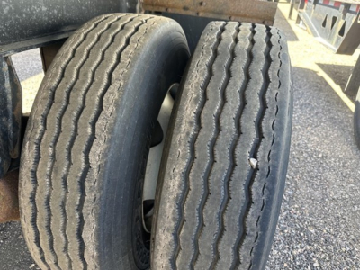 Rear view of Fontaine trailer with dual tires, tread wear visible, part of flatbed chassis and deck rails.