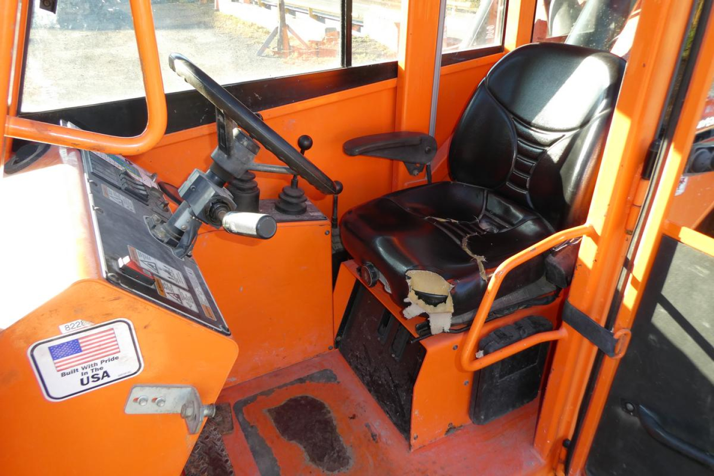 Cab interior of a JLG 8042 telescopic lift showing operator seat, steering wheel, control lever, and orange frame.