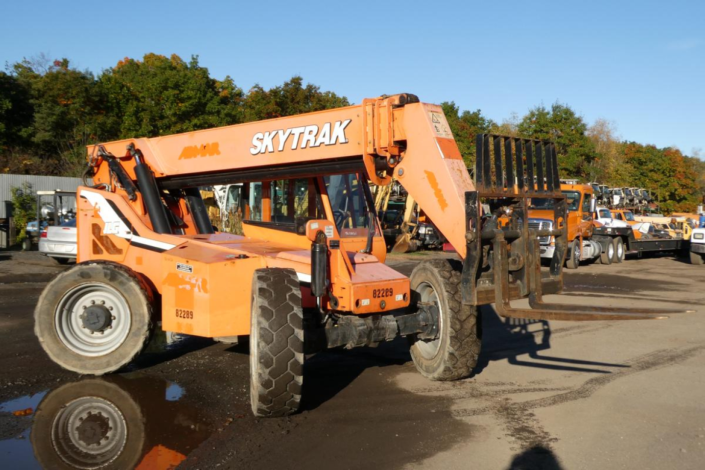 SkyTrak telescopic forklift in yard with orange paint and black forks; visible text includes SKYTRAK on upper boom and 82289/center chassis numbers on side.