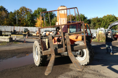 JLG 8042 telescopic lift with forks in foreground, orange machinery, working height components, rugged tires, outdoor lot.