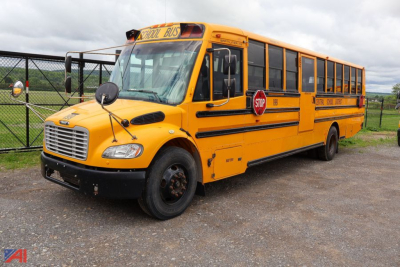 Yellow Freightliner school bus with black bumper and stop sign, side windows, bus doors, and 'SCHOOL BUS' sign on the roof; worn wheel hubcaps and chain-link fence in background.
