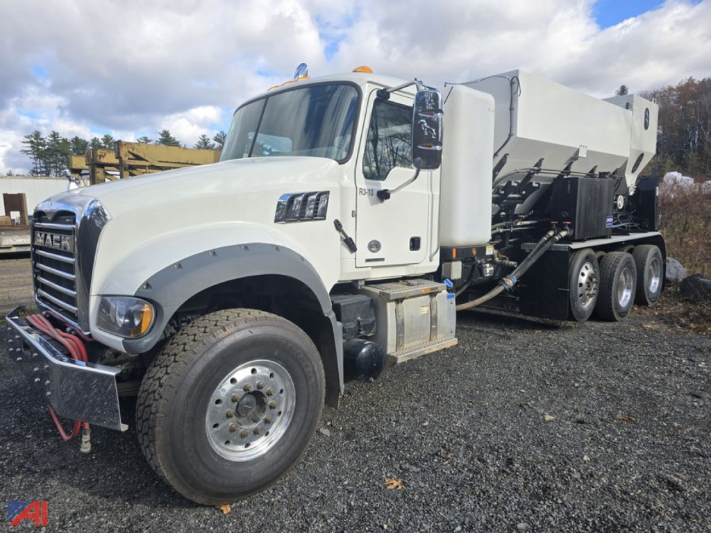 Truck cab and volumetric concrete mixer body on a white Mack Granite GR64F, side view showing chassis and wheels, gray mixer drum, front bumper with winch lines.