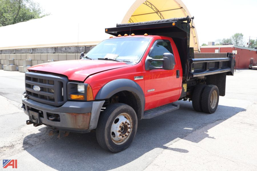 Ford F-450 Super Duty dump truck with plow showing front and right side, red cab, black grille, dual rear wheels, dump bed, with snow plow attachment in yellow behind cab.