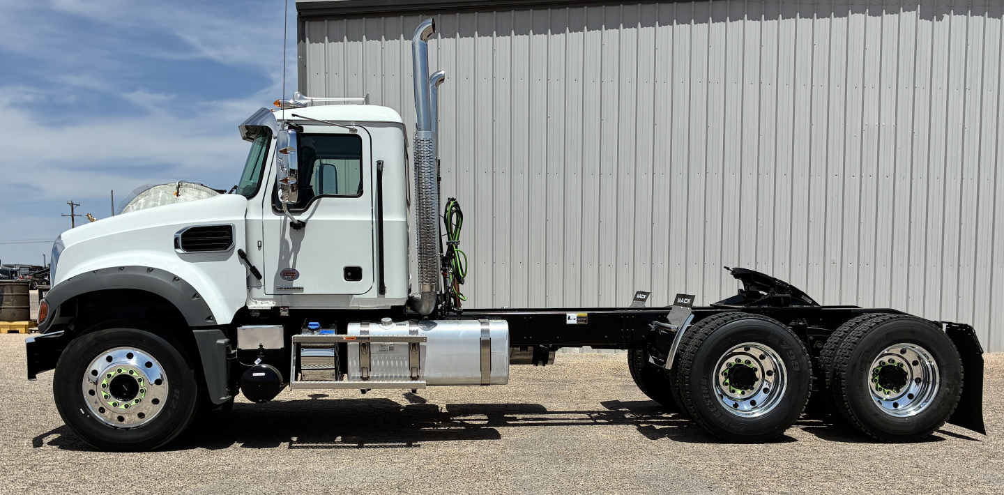Mack GR64FT conventional daycab tractor side view showing long axle with dual rear axles and fuel tanks, white cab, chrome steps, large front wheel, metallic frame.