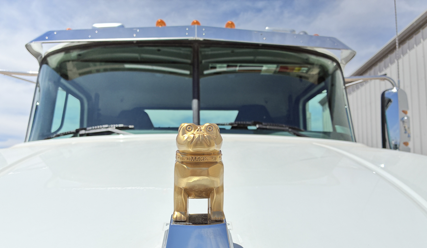 Front view of a Mack truck hood ornament on the nose with windshield and cab in background.