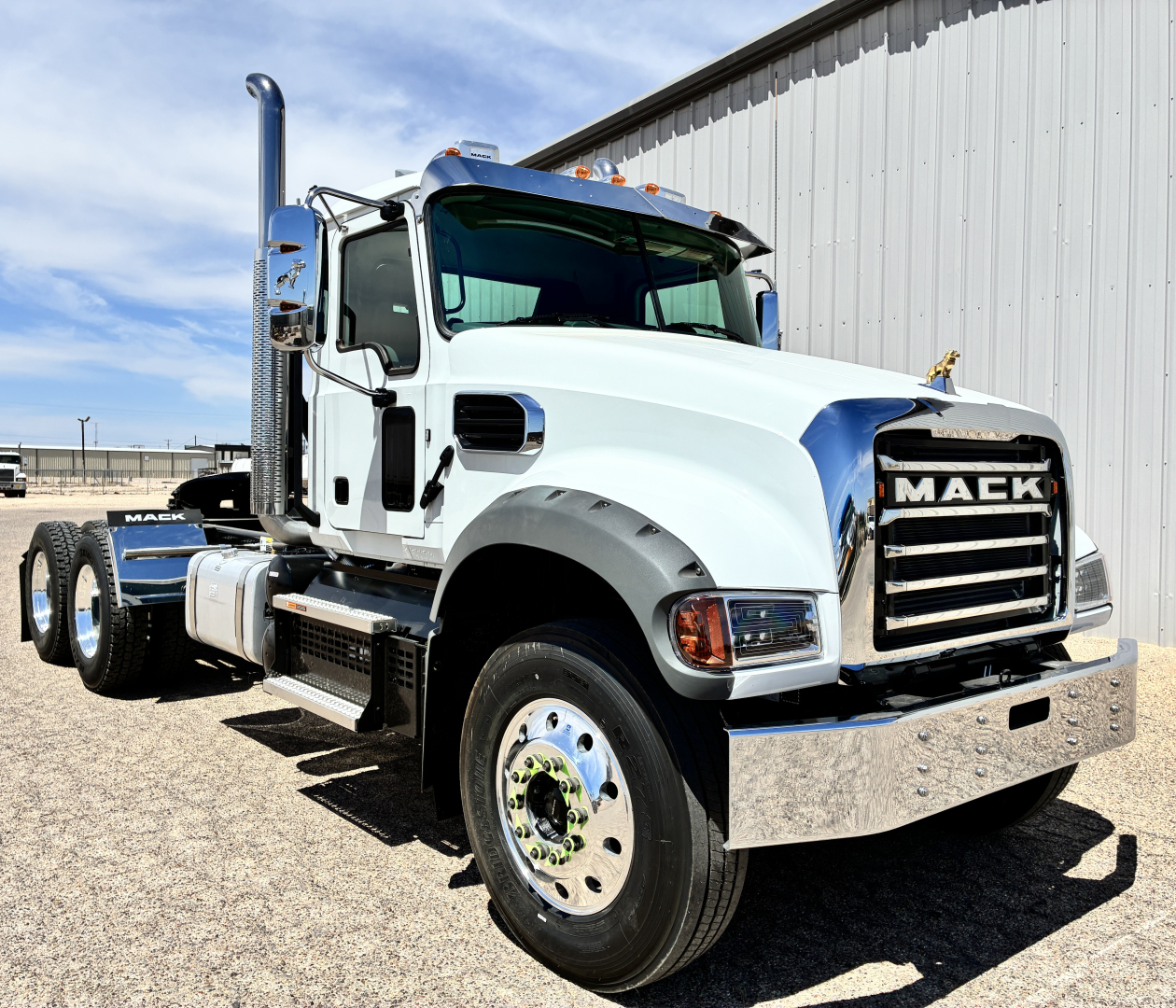 Mack GR64FT conventional daycab truck front-left view showing chrome grille, white cab, dual rear axles, fuel tanks, and chrome bumper.