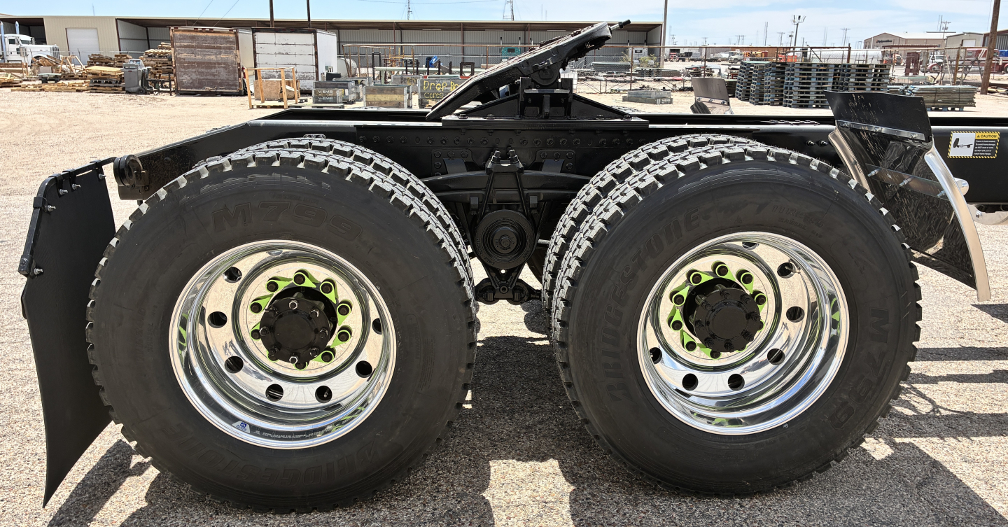 Two rear axles of a new Mack GR64FT tractor showing dual-tire setup with chrome rims and green lug nut accents.