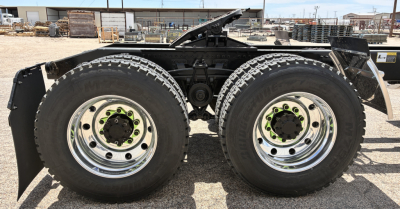 Two rear axles of a new Mack GR64FT tractor showing dual-tire setup with chrome rims and green lug nut accents.