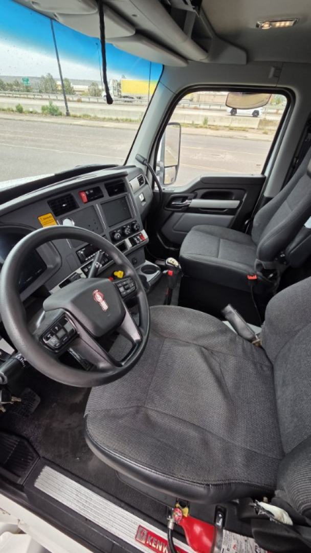 Kenworth T880 truck cab interior showing steering wheel and driver seat viewed from door, dashboard gauges, and center console.