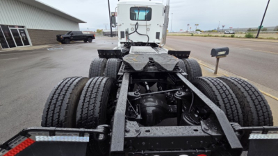 Kenworth T880 chassis showing dual rear axles and frame with hydraulic lines, fifth wheel, and cab in background.