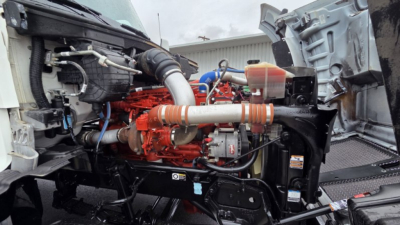 Kenworth T880 engine bay showing bright orange engine and intake with hoses, surrounding chassis, and front cab components.
