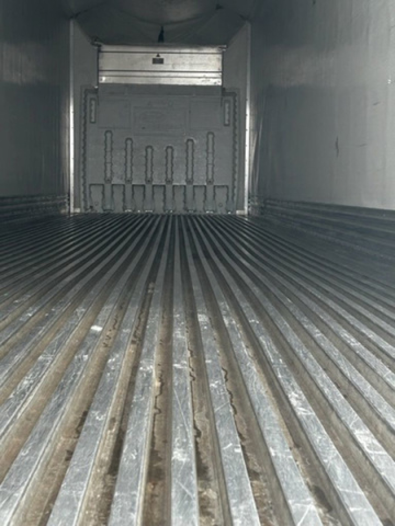 Interior of a refrigerated trailer with ribbed floor leading to a rear door. No legible labels or text visible.