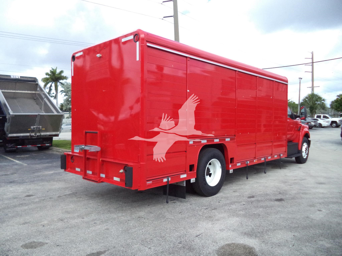 Red service truck body with white bird graphic on side, rear view showing storage compartments and mud flaps, Ford F-650 utility truck in a dealership lot.