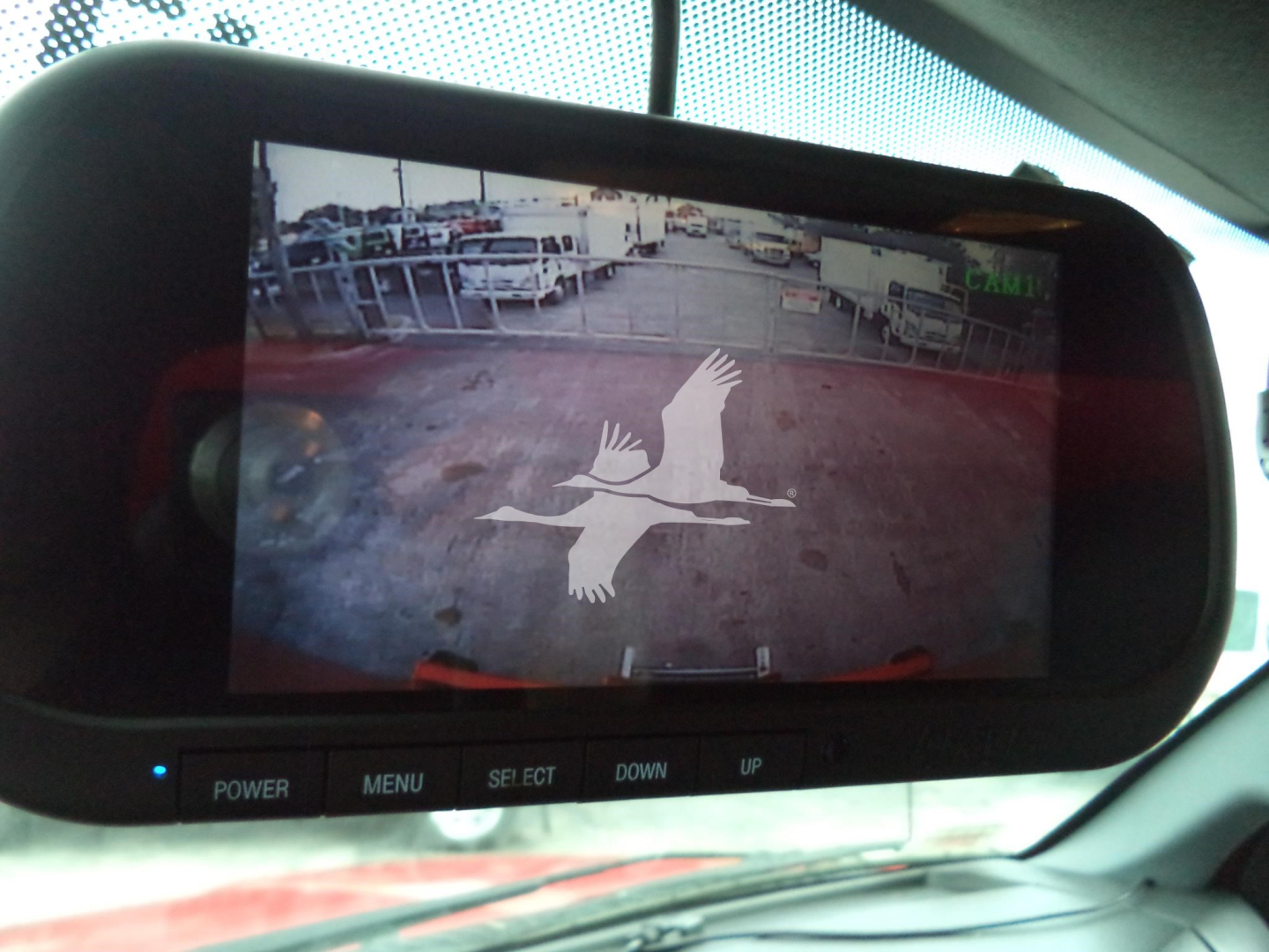Rear-view display showing mirrored image of a truck yard with a large white bird logo overlayed on the screen.