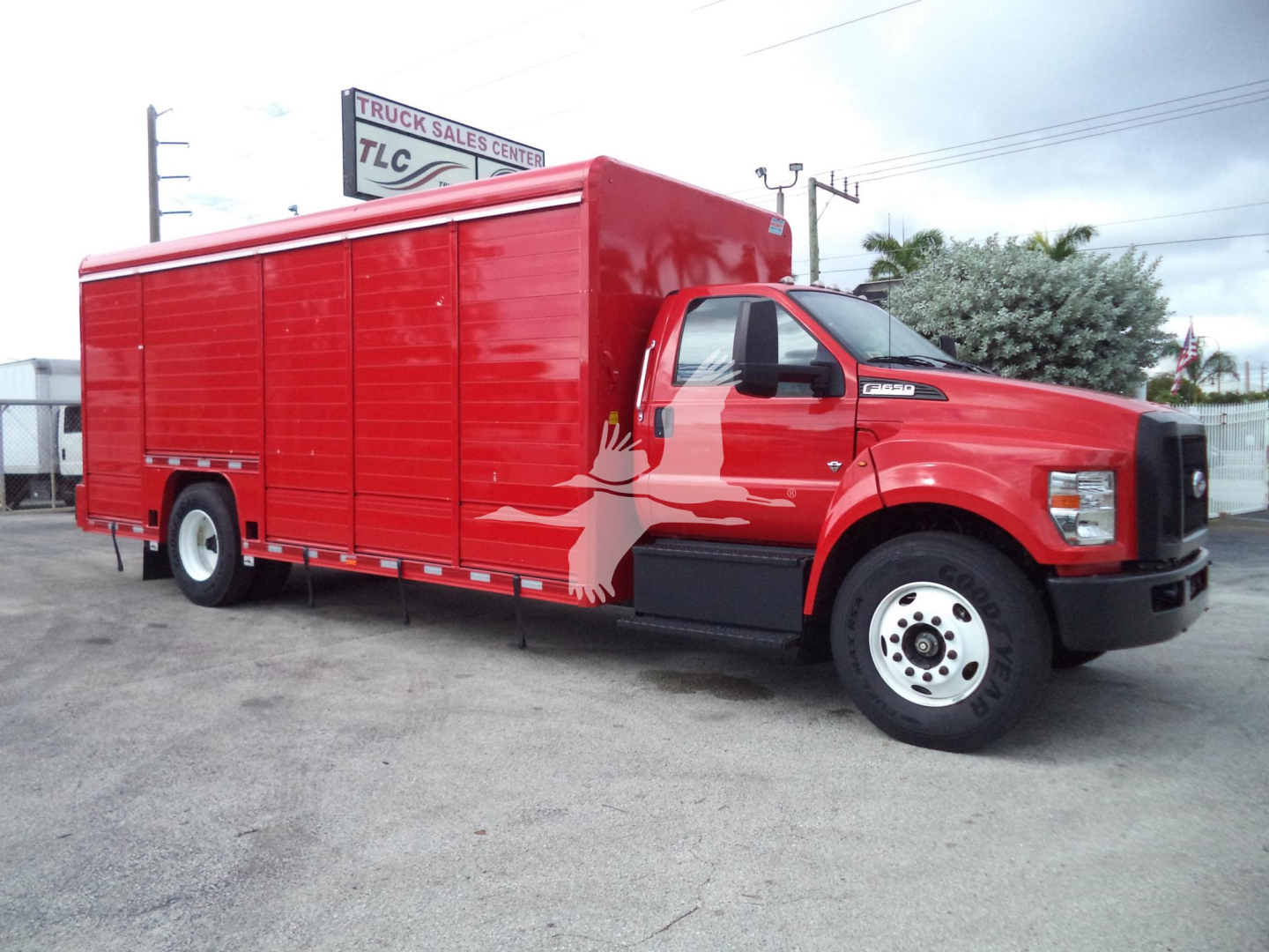 Ford F-650 utility truck with red cargo body and painted bird graphic on the side, showing a large cab and utility compartments.
