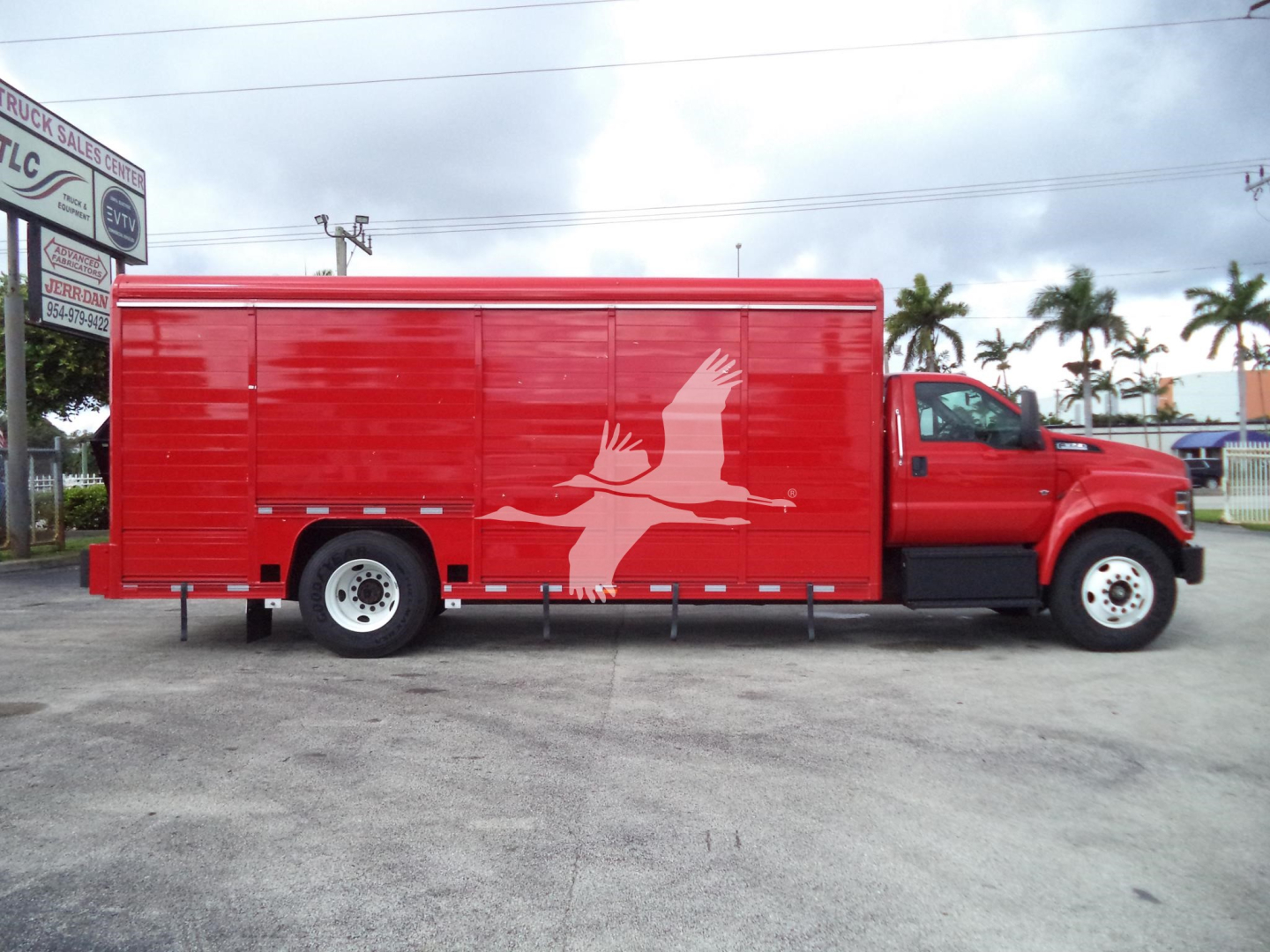 Red Ford F-650 utility truck with a large cargo box and a white bird graphic on the side, in a parking lot.