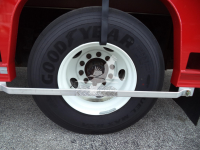 Goodyear tire mounted on white wheel in red truck wheel well with hanging strap and chrome step plate.