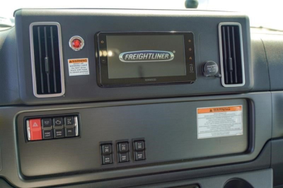 Freightliner 114SD dashboard showing center touchscreen with Freightliner logo, air vents on sides, warning labels, and control buttons.
