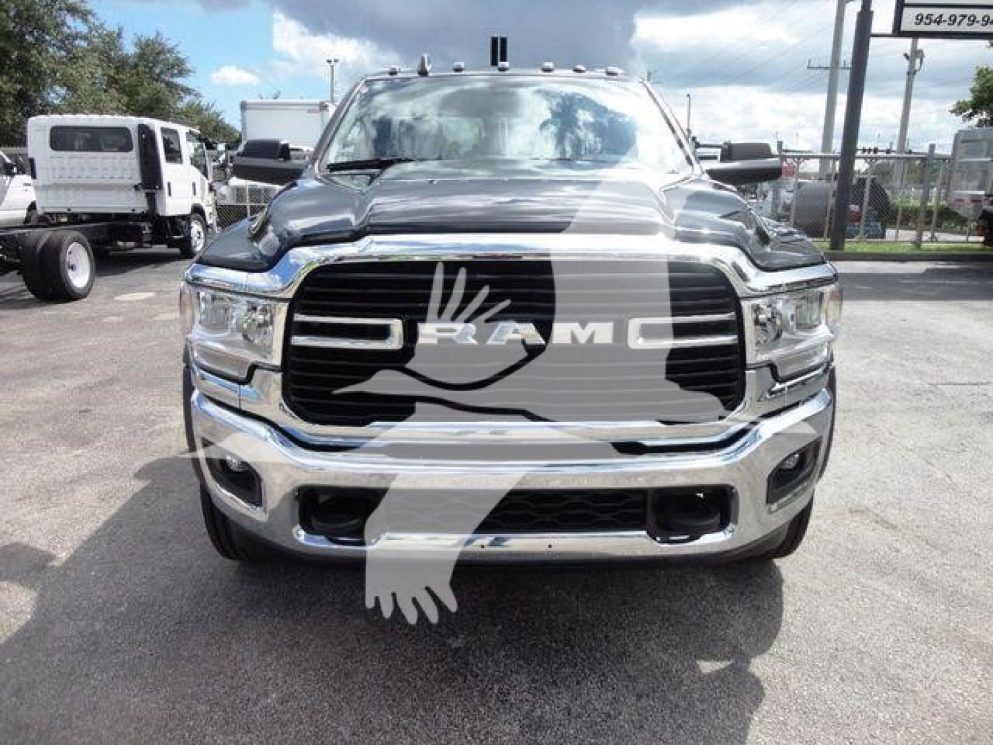 Ram truck front view showing bold grille with RAM lettering, chrome bumper, and dual headlights in a showroom lot.