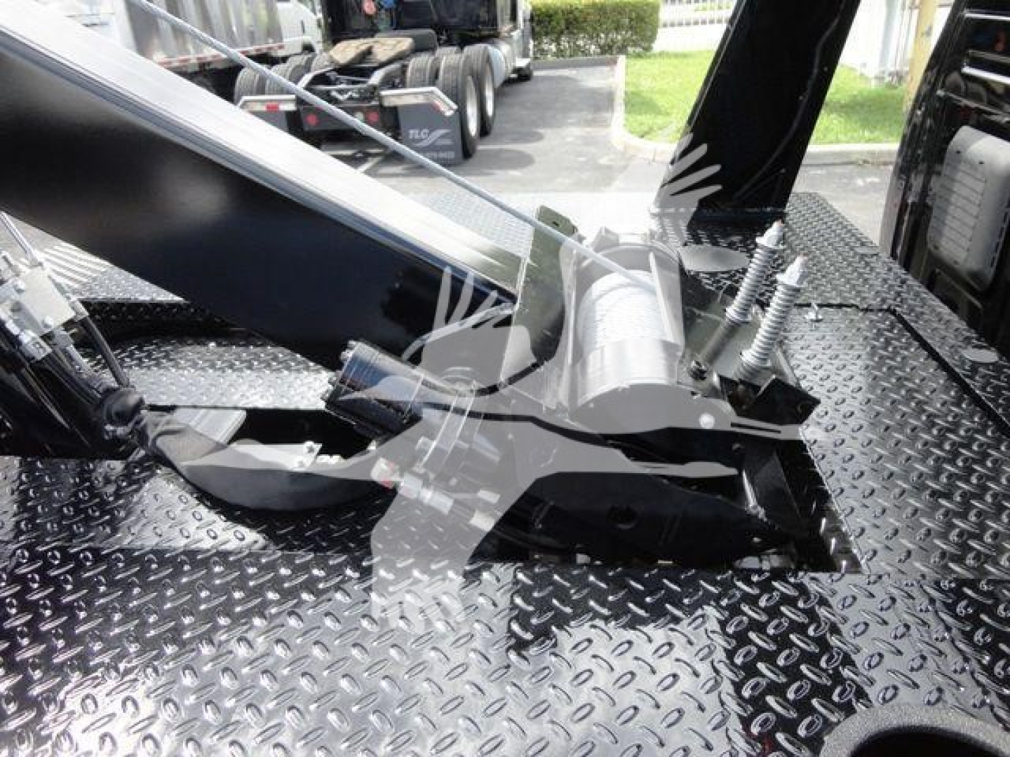 Winch mounting assembly on a flatbed truck with hydraulic winch drum and cables visible, mounted on diamond plate bed.