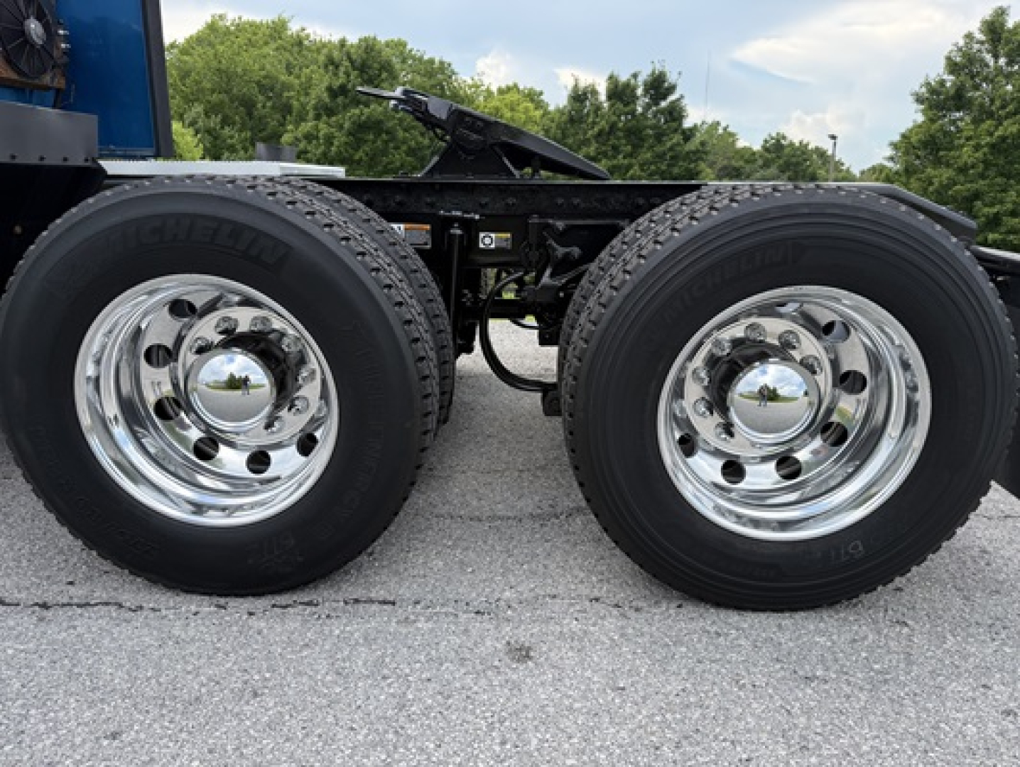 Twin rear axles of a Peterbilt 579 truck with chrome wheels and Michelin tires; no visible text on tires; chassis rails and air brake lines between axles.