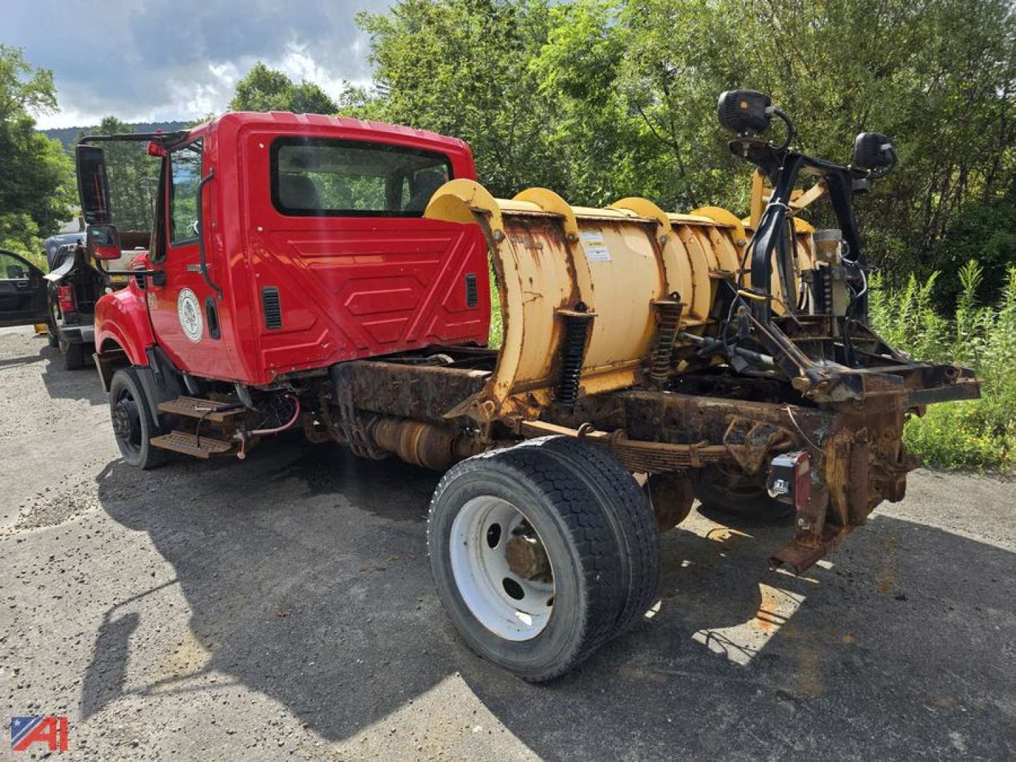 Cab and chassis truck with snow plow mount on rear, red cab, large yellow plow housing, single rear axle, parked on dirt.
