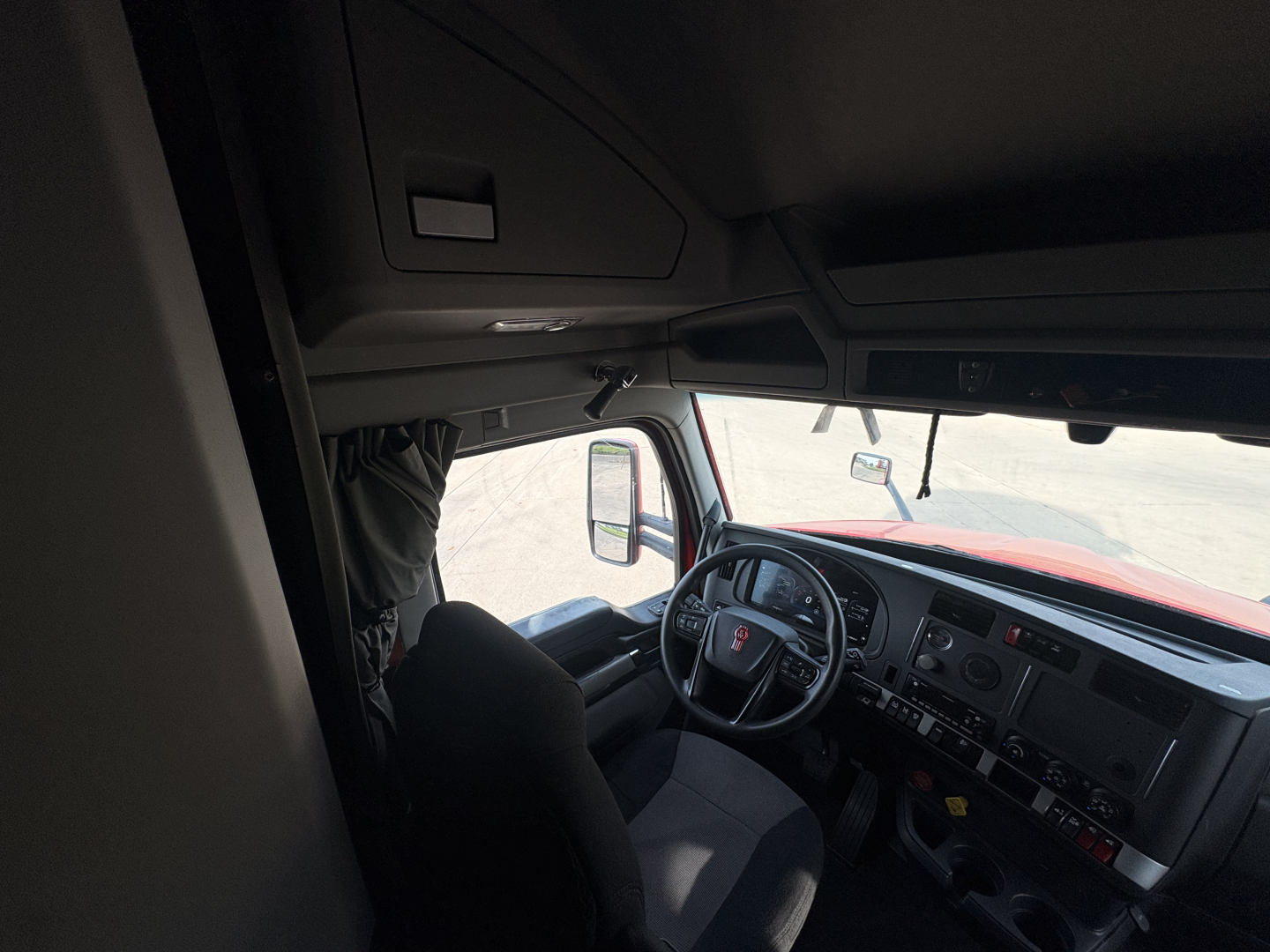Truck cab interior of a Kenworth T680 2023 showing steering wheel and dashboard from passenger side with center console and driver seat.